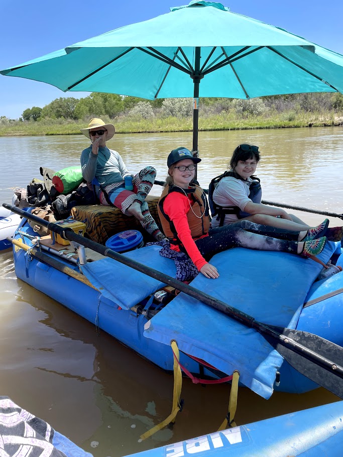A picture of Josh, KK and Rylen on the raft under the umbrella